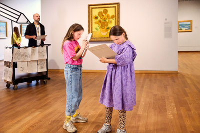 Twee meisjes zijn aan het tekenen voor het schilderij Zonnebloemen van Van Gogh in het Van Gogh Museum. Naast het schilderij staat de Tekenkar. foto: Suzanne Karsters
